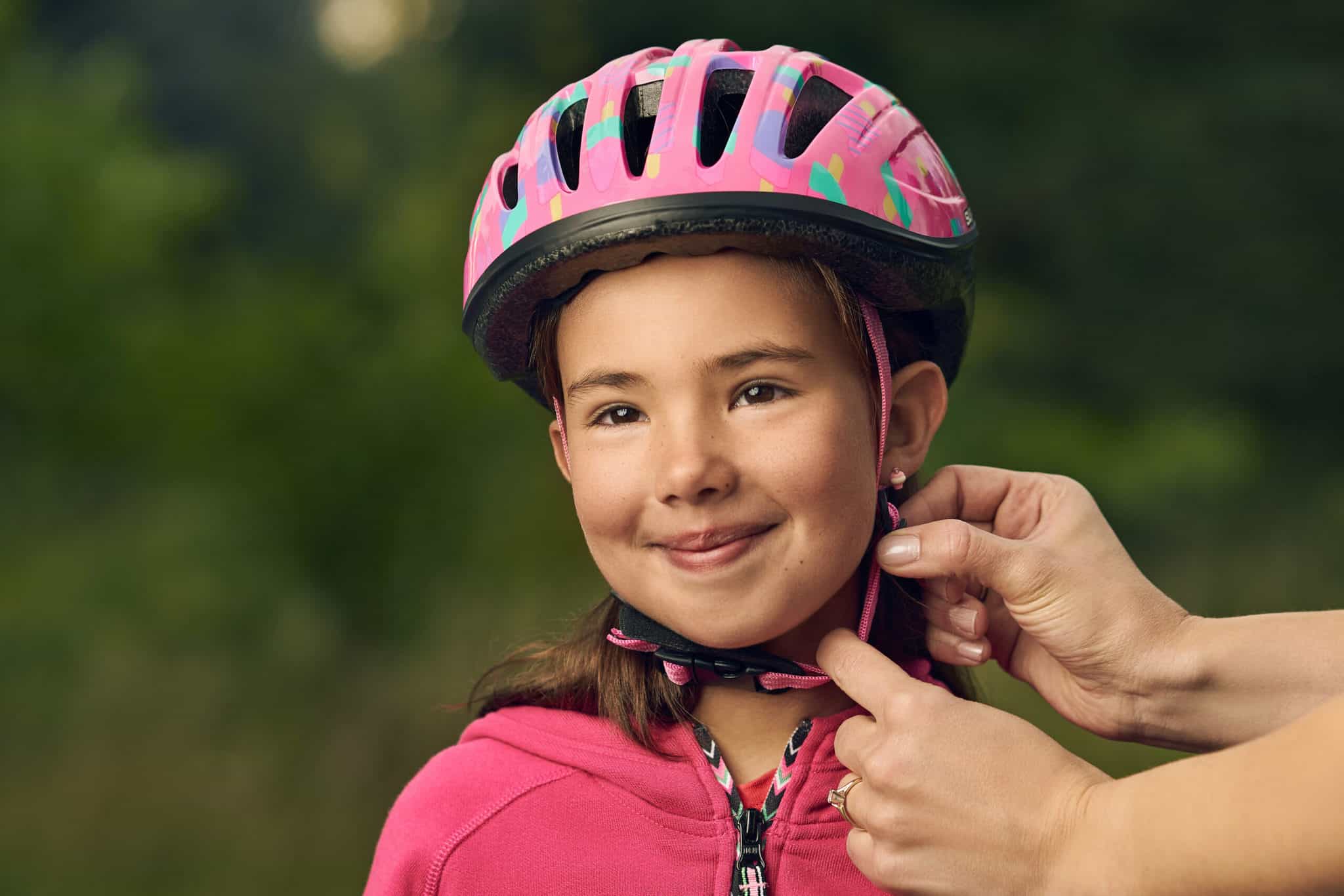 A young girl gets a bicycle helmet put on by an off-camera adult.