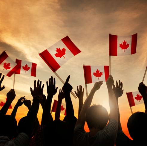 Silhouettes of people with their hands in the air holding Canadian flags.